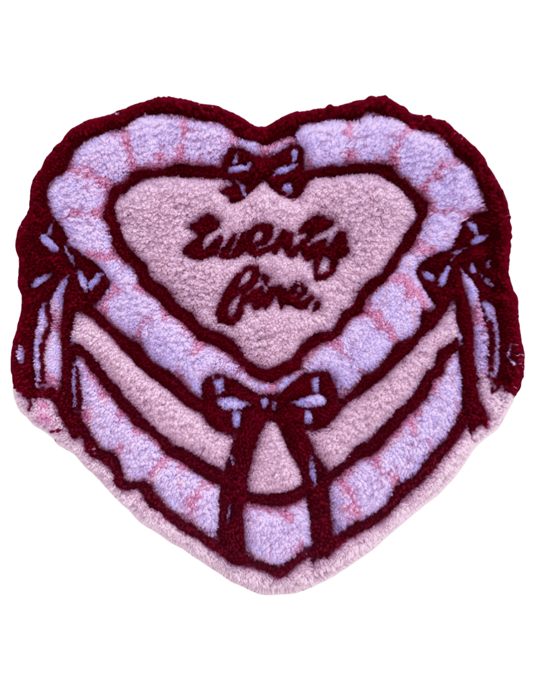A heart-shaped rug in pastel pink and lavender with a checkered pattern, maroon trim, and delicate bow details framing a hand-tufted 'twenty five' script. A sweet custom milestone piece.